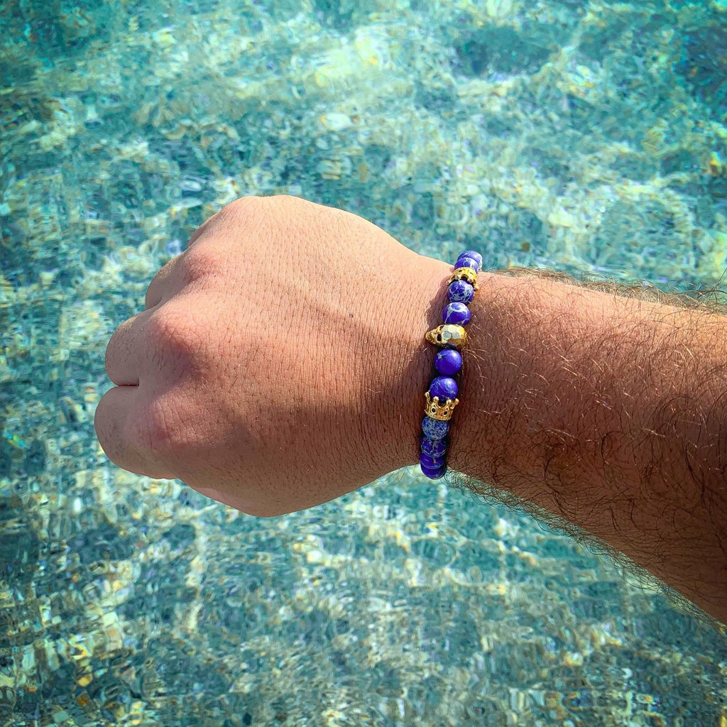 blue mens beaded bracelet with gold skull on wrist at beach over water